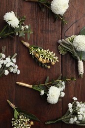 Small stylish boutonnieres on wooden table, flat lay