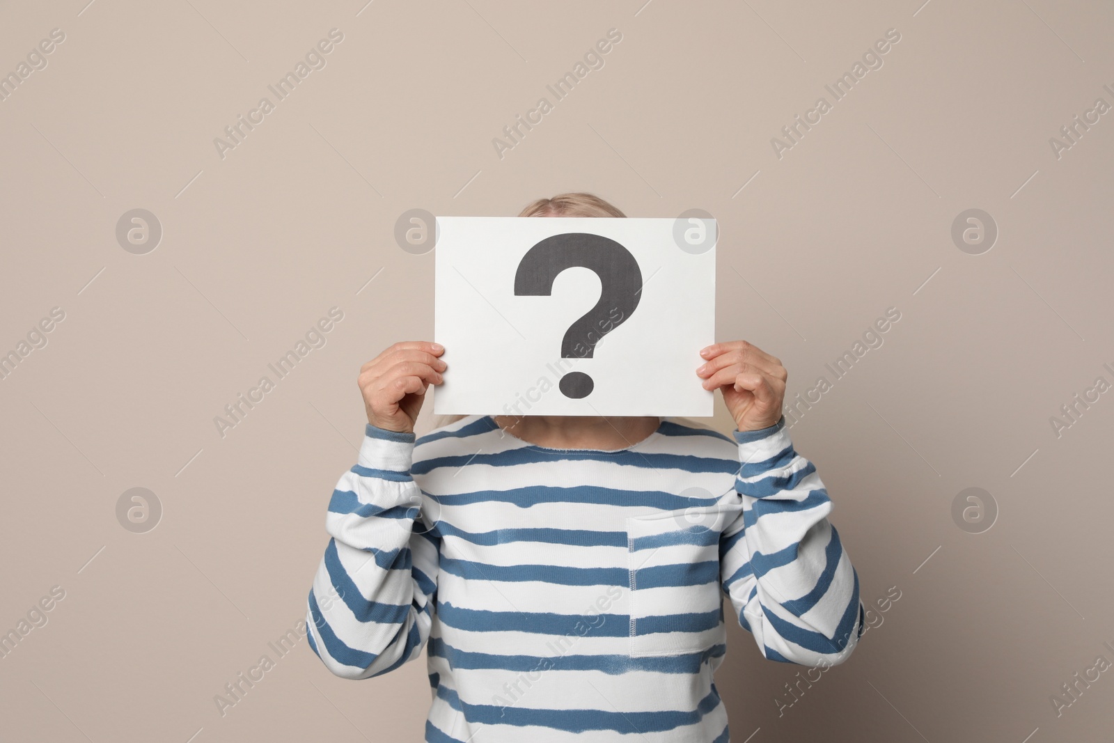 Photo of Mature woman holding paper with question mark on beige background