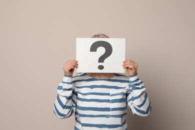 Photo of Mature woman holding paper with question mark on beige background