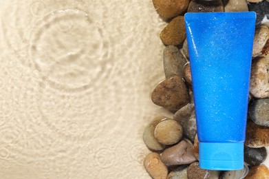 Tube of face cleansing product and stones in water against beige background, flat lay. Space for text