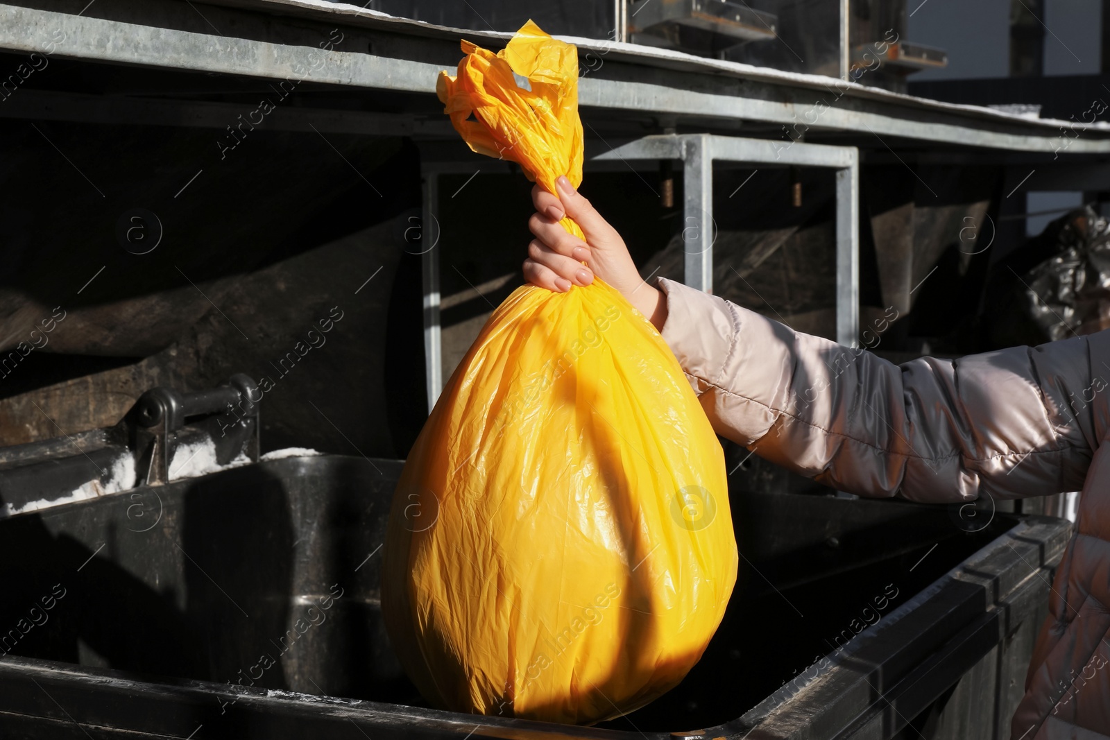 Photo of Woman throwing trash bag full of garbage in bin outdoors, closeup