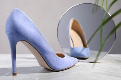 Photo of Stylish high heeled shoe in front of mirror on grey table. Vanity concept