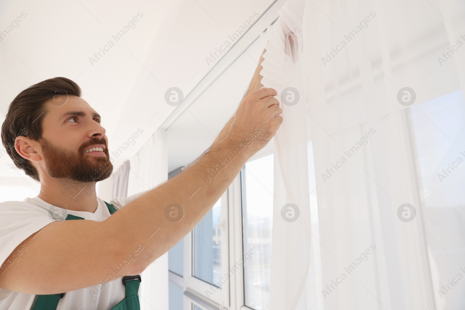 Photo of Worker in uniform hanging window curtain indoors