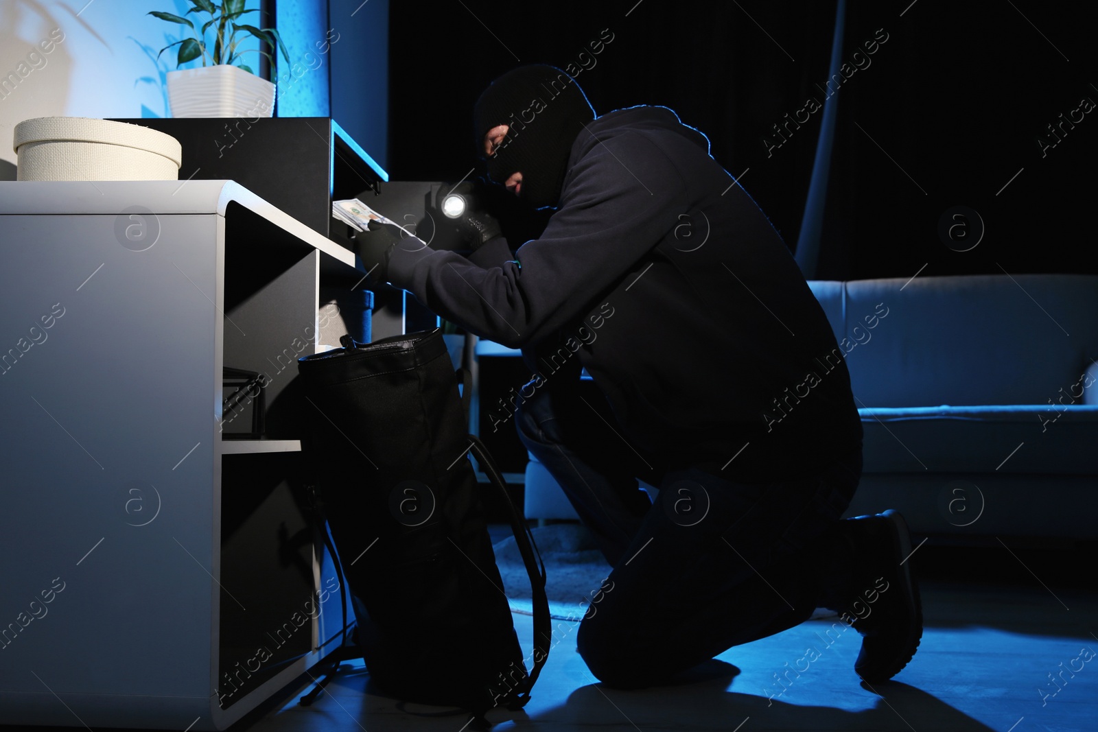 Photo of Thief taking money out of steel safe indoors at night