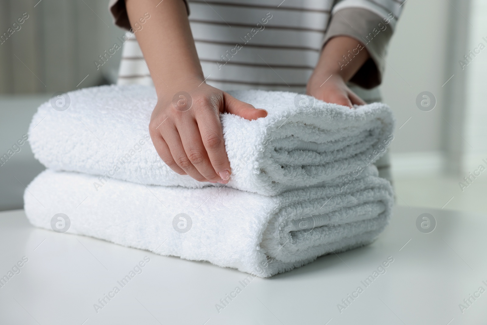 Photo of Woman touching soft white towel indoors, closeup