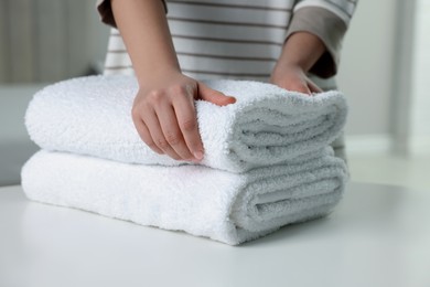 Woman touching soft white towel indoors, closeup