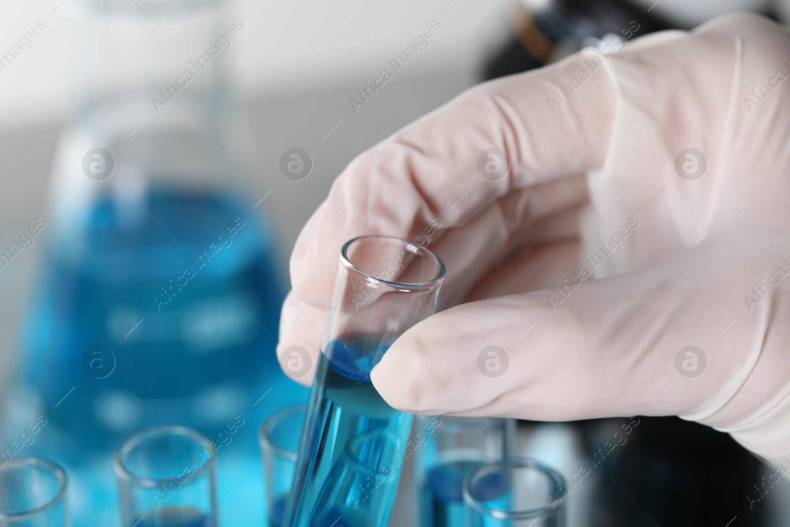 Photo of Scientist taking test tube with light blue liquid in laboratory, closeup