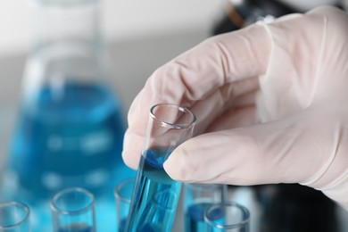 Scientist taking test tube with light blue liquid in laboratory, closeup