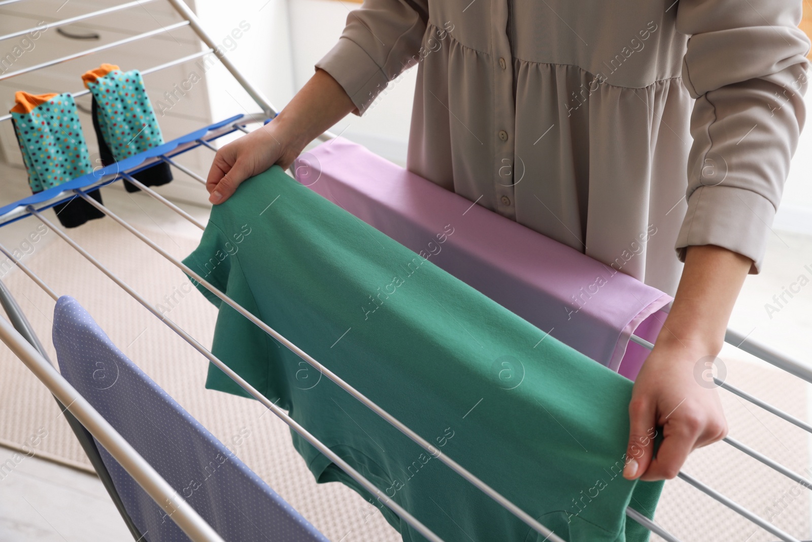 Photo of Young woman hanging clean laundry on drying rack at home, closeup