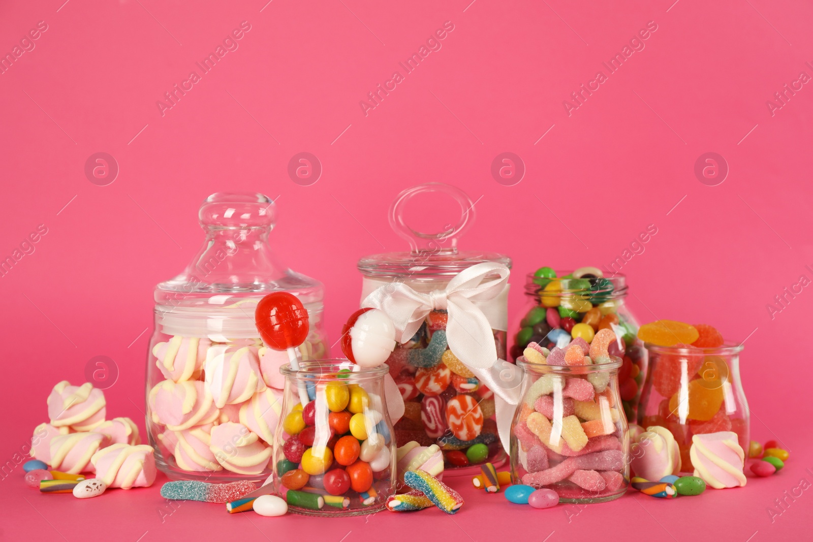 Photo of Glass jars with lots of different candies on bright pink background