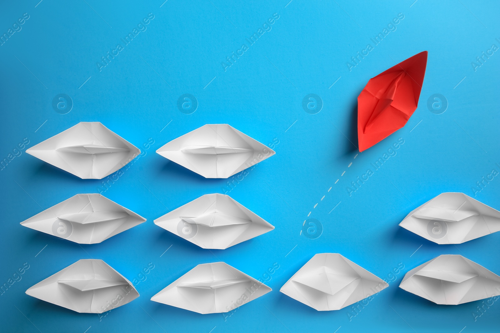 Photo of Red paper boat floating away from others on light blue background, flat lay. Uniqueness concept