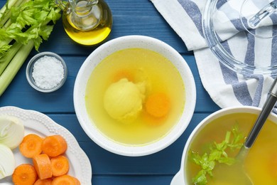 Photo of Delicious chicken bouillon and ingredients on blue wooden table, flat lay