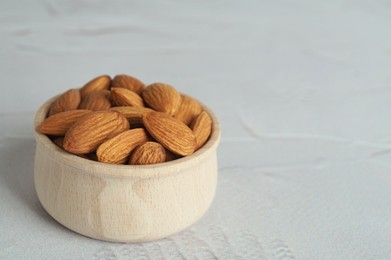 Tasty almonds in wooden bowl on white table, space for text