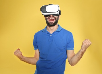 Photo of Emotional young man playing video games with virtual reality headset on color background