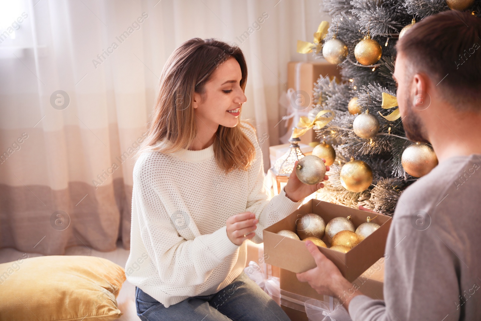 Image of Happy couple decorating Christmas tree together at home