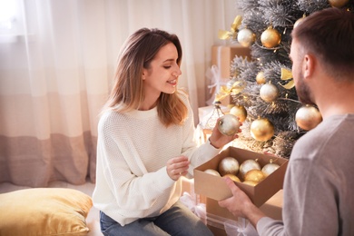 Image of Happy couple decorating Christmas tree together at home