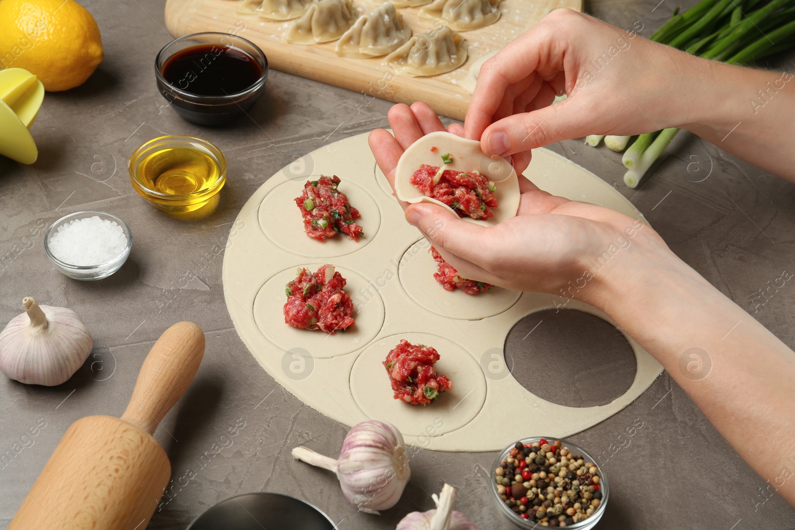 Photo of Woman cooking delicious gyoza at light grey table, closeup