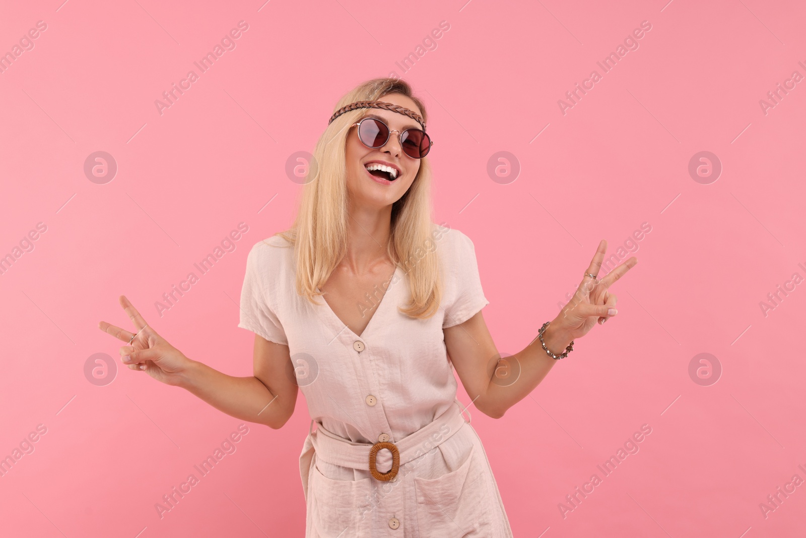 Photo of Portrait of smiling hippie woman showing peace signs on pink background