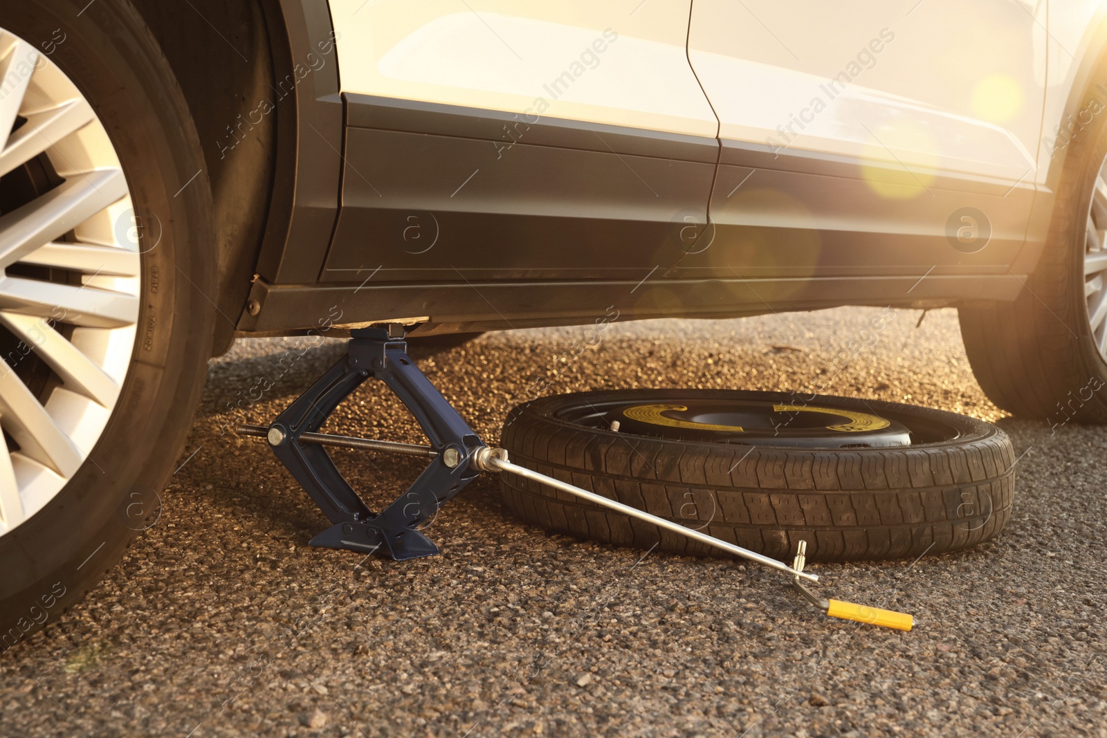 Photo of Car lifted by scissor jack and spare wheel on roadside