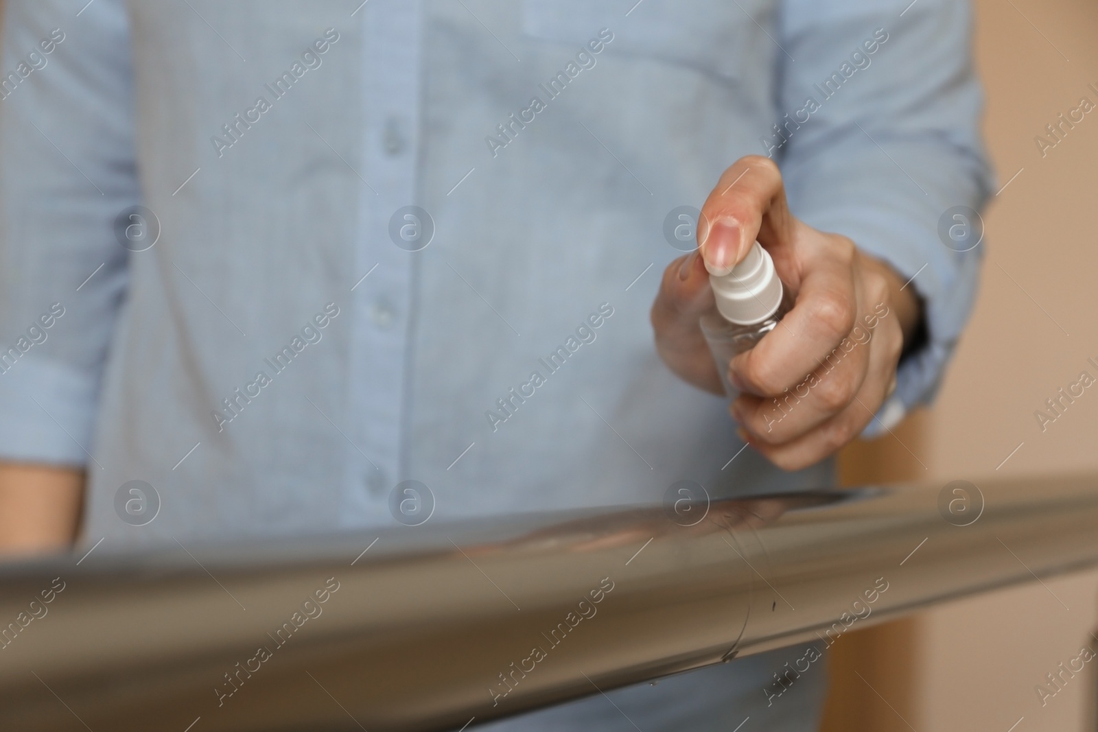 Photo of Woman spraying antiseptic onto metal railing indoors, closeup