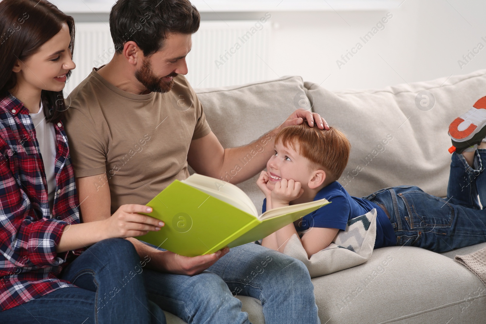 Photo of Happy parents with their child reading book on couch at home