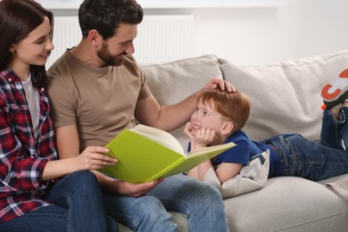 Happy parents with their child reading book on couch at home