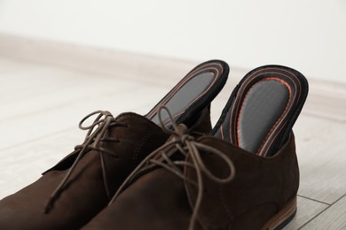 Photo of Orthopedic insoles in shoes on floor, closeup