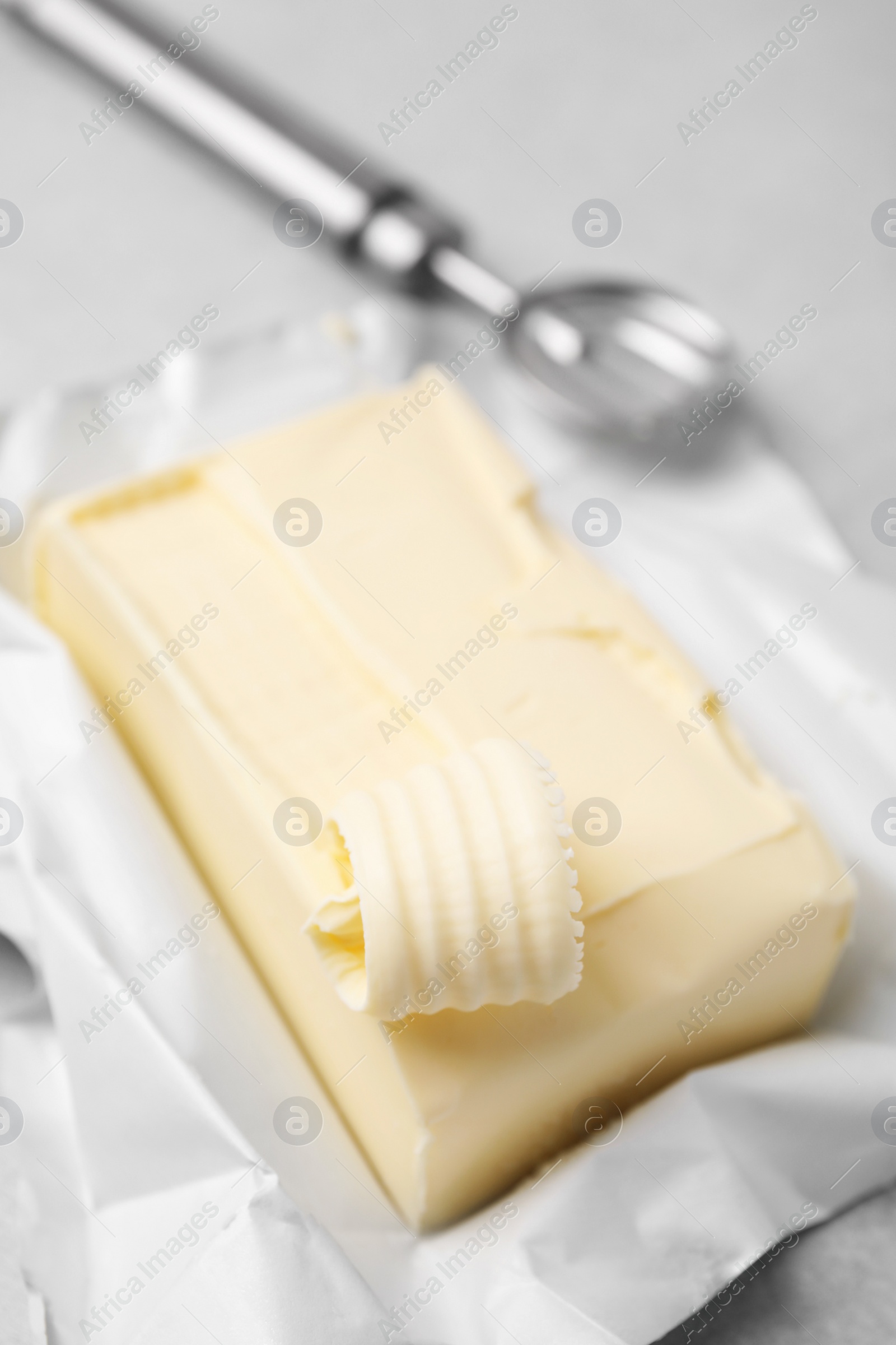 Photo of Tasty butter with curl and spoon on light grey table, closeup