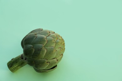 Photo of Whole fresh raw artichoke on green background, top view. Space for text