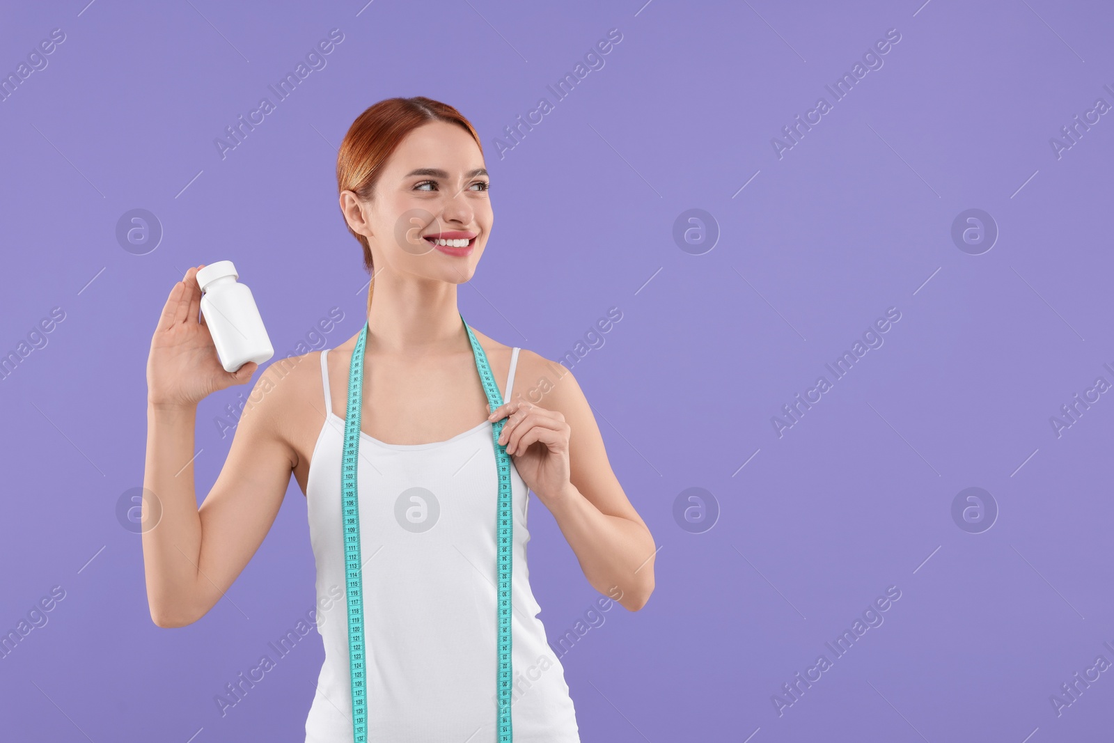 Photo of Happy young woman with bottle of pills and measuring tape on purple background, space for text. Weight loss