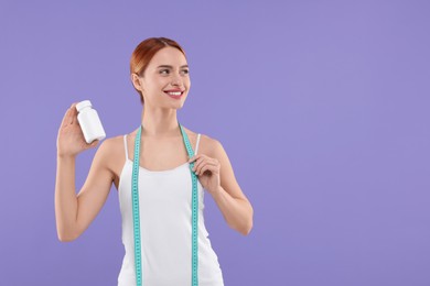 Photo of Happy young woman with bottle of pills and measuring tape on purple background, space for text. Weight loss