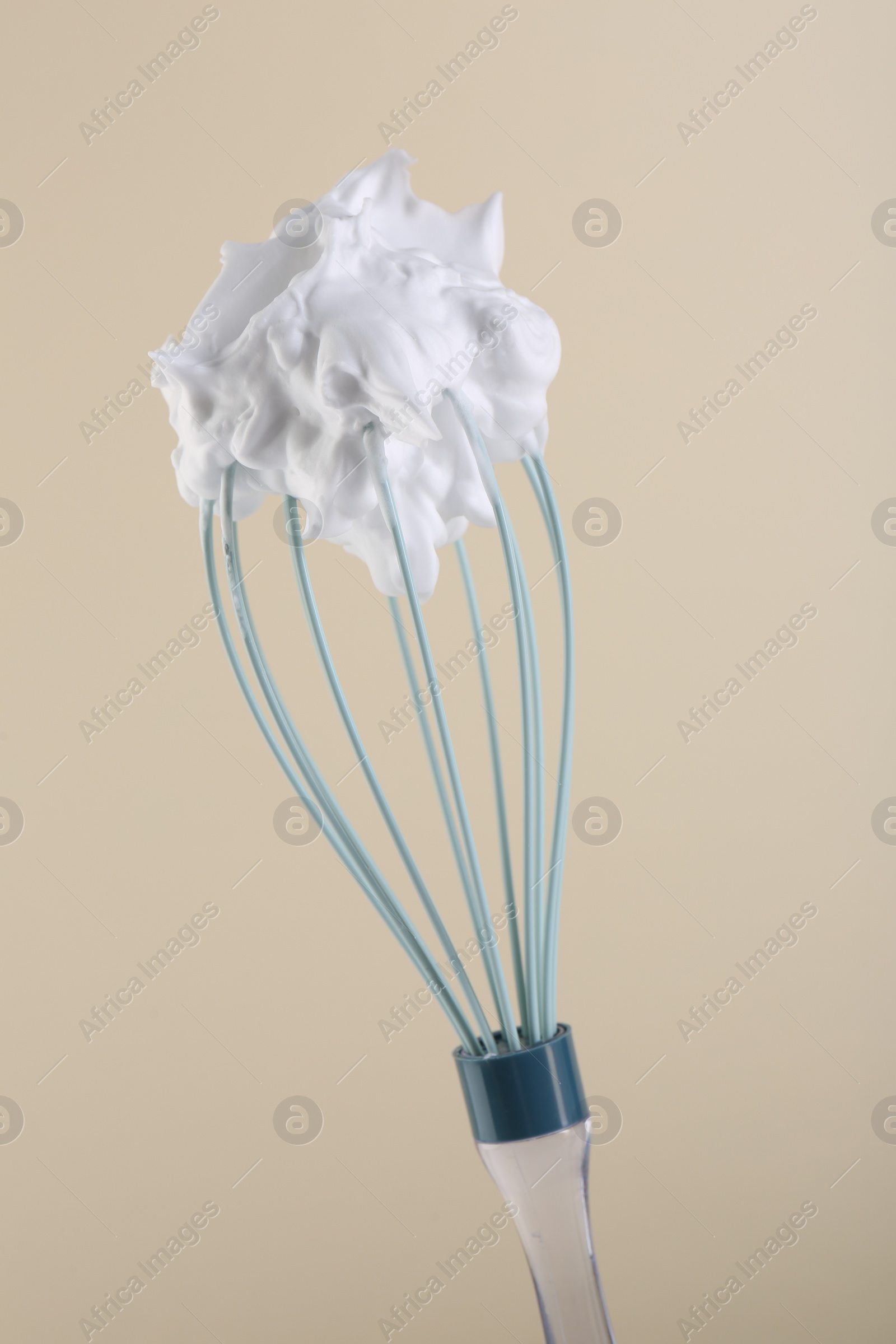 Photo of Whisk with whipped cream on beige background