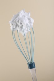 Whisk with whipped cream on beige background