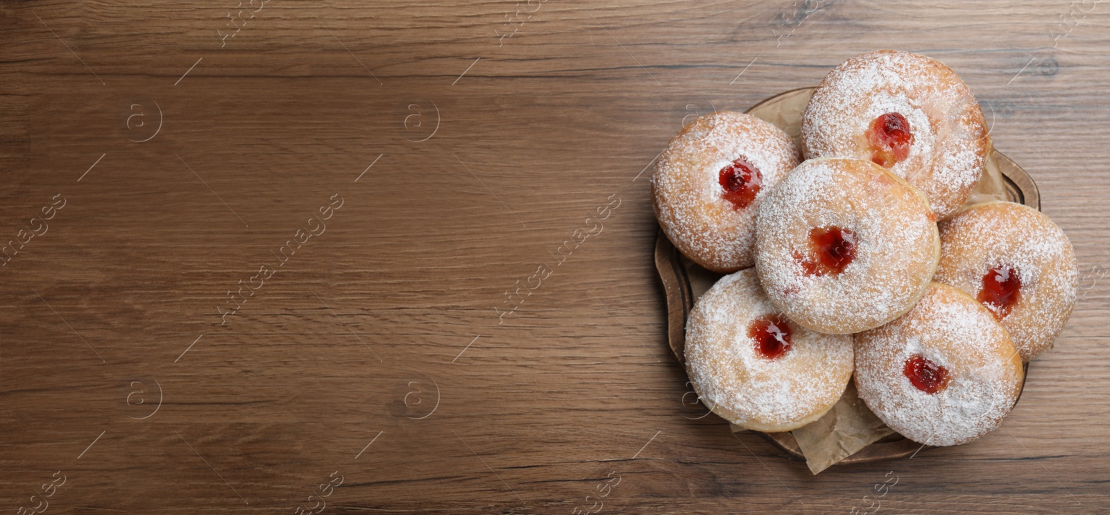 Photo of Delicious donuts with jelly and powdered sugar on wooden table, top view. Space for text