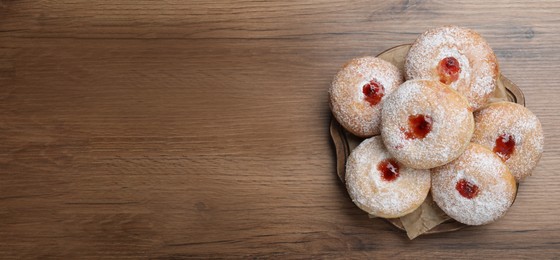 Delicious donuts with jelly and powdered sugar on wooden table, top view. Space for text