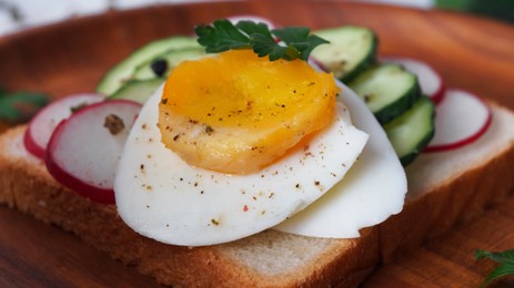 Tasty sandwich with boiled egg, radish and cucumber on wooden plate, closeup