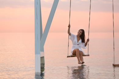 Young woman enjoying sunrise on swing over water