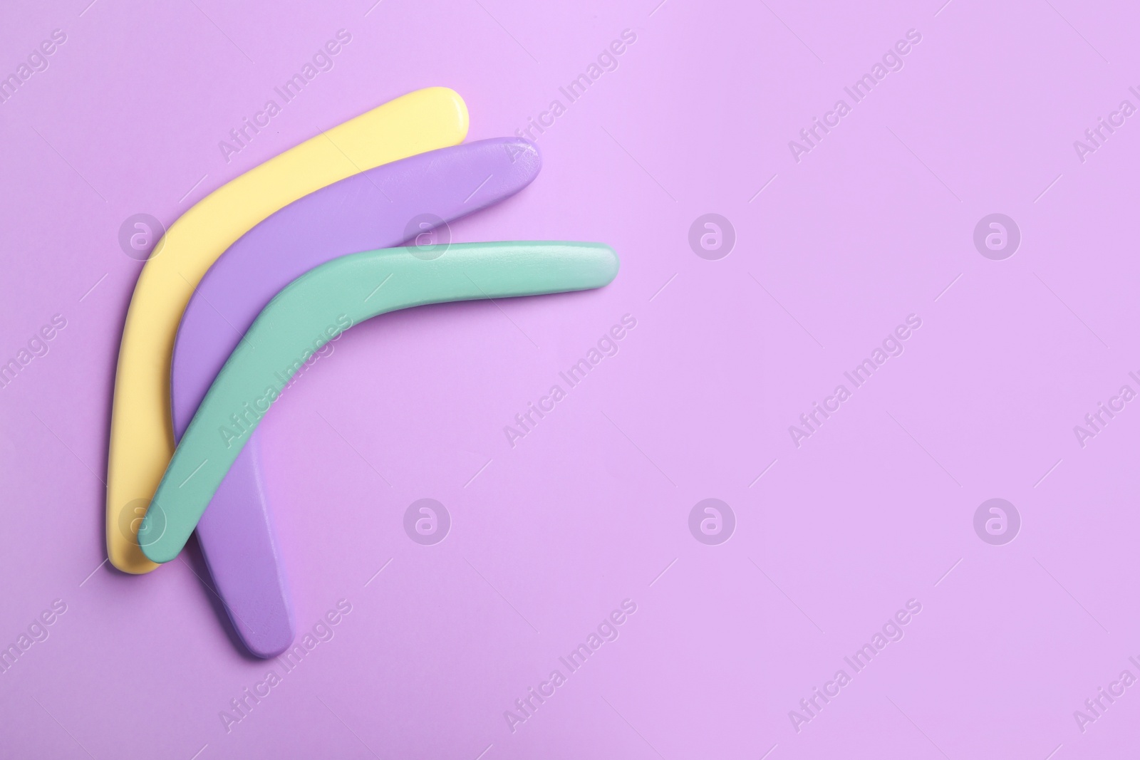 Photo of Colorful wooden boomerangs on lilac background, flat lay. Space for text