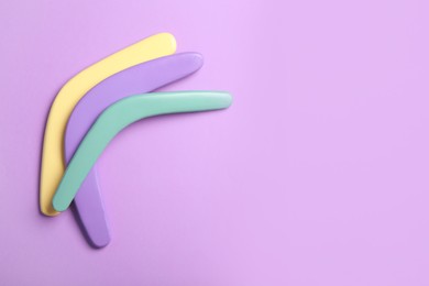 Colorful wooden boomerangs on lilac background, flat lay. Space for text