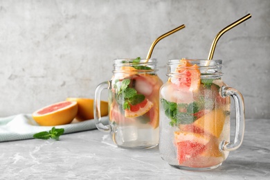 Photo of Mason jars of refreshing drink with grapefruit and mint on grey stone table, space for text