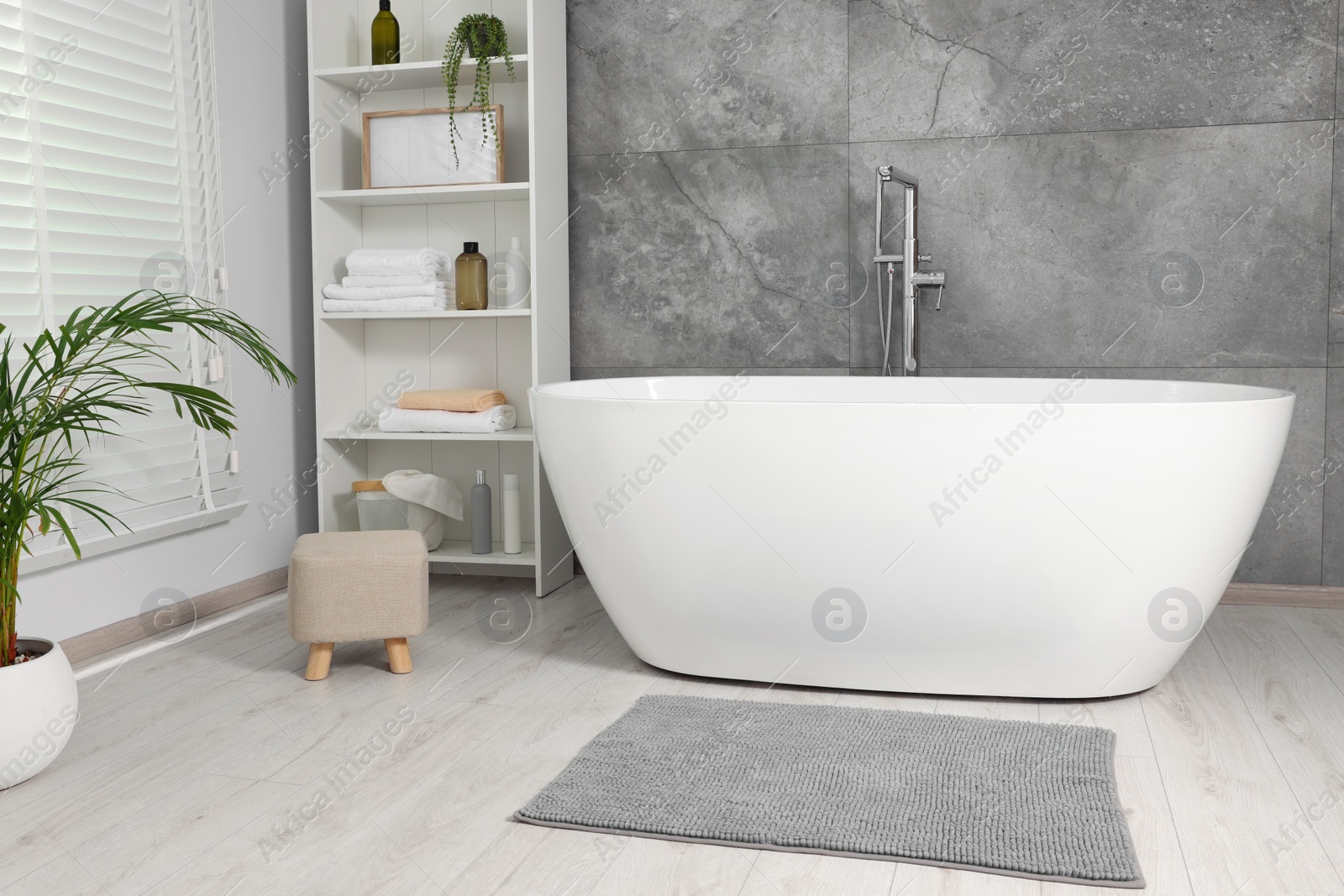 Photo of Stylish bathroom interior with ceramic tub, care products and towels in cabinet