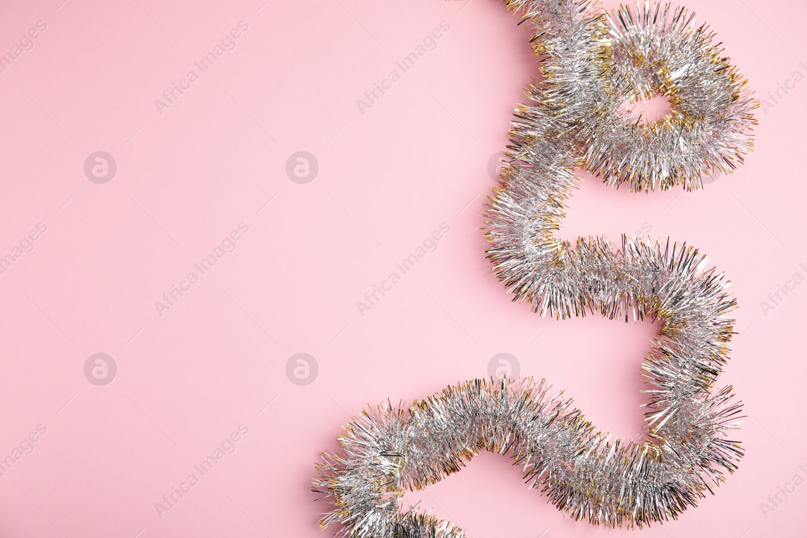 Photo of Sparkling tinsel on pink background, top view. Space for text