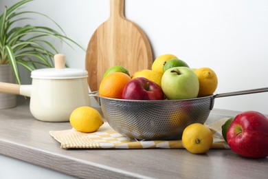 Photo of Metal colander with different fruits on countertop in kitchen