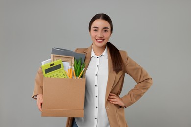 Photo of Happy unemployed woman holding box with personal office belongings on grey background