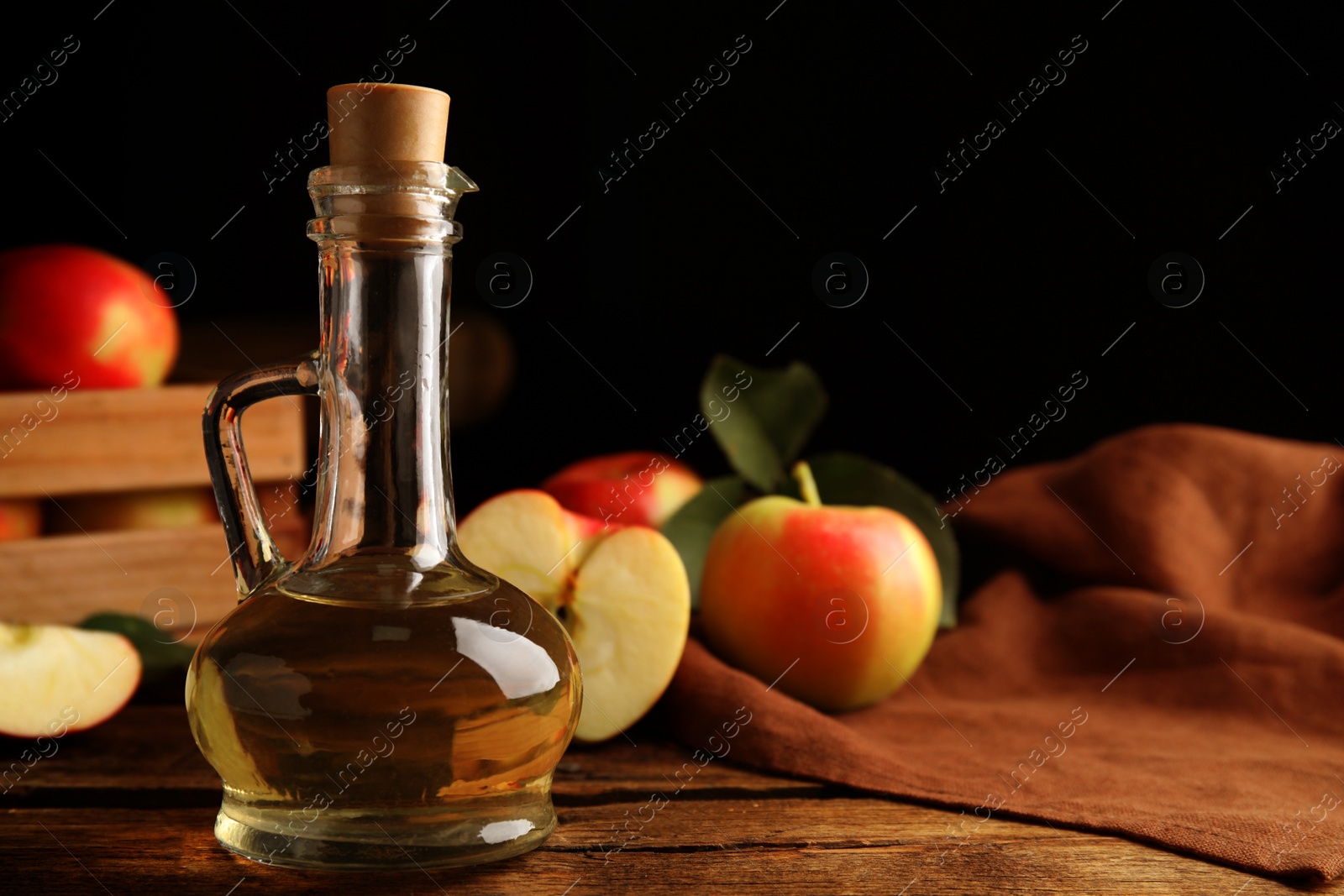 Photo of Natural apple vinegar and fresh fruits on wooden table. Space for text