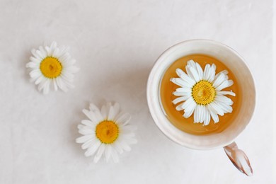Tasty herbal tea and fresh chamomile flowers on white table, flat lay