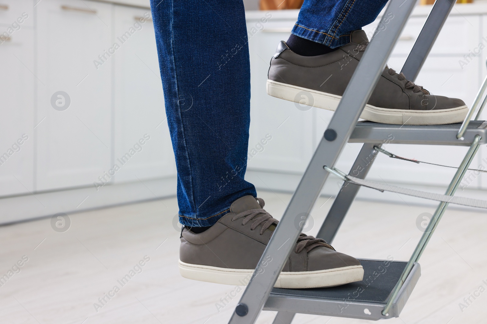 Photo of Man climbing up metal stepladder indoors, closeup