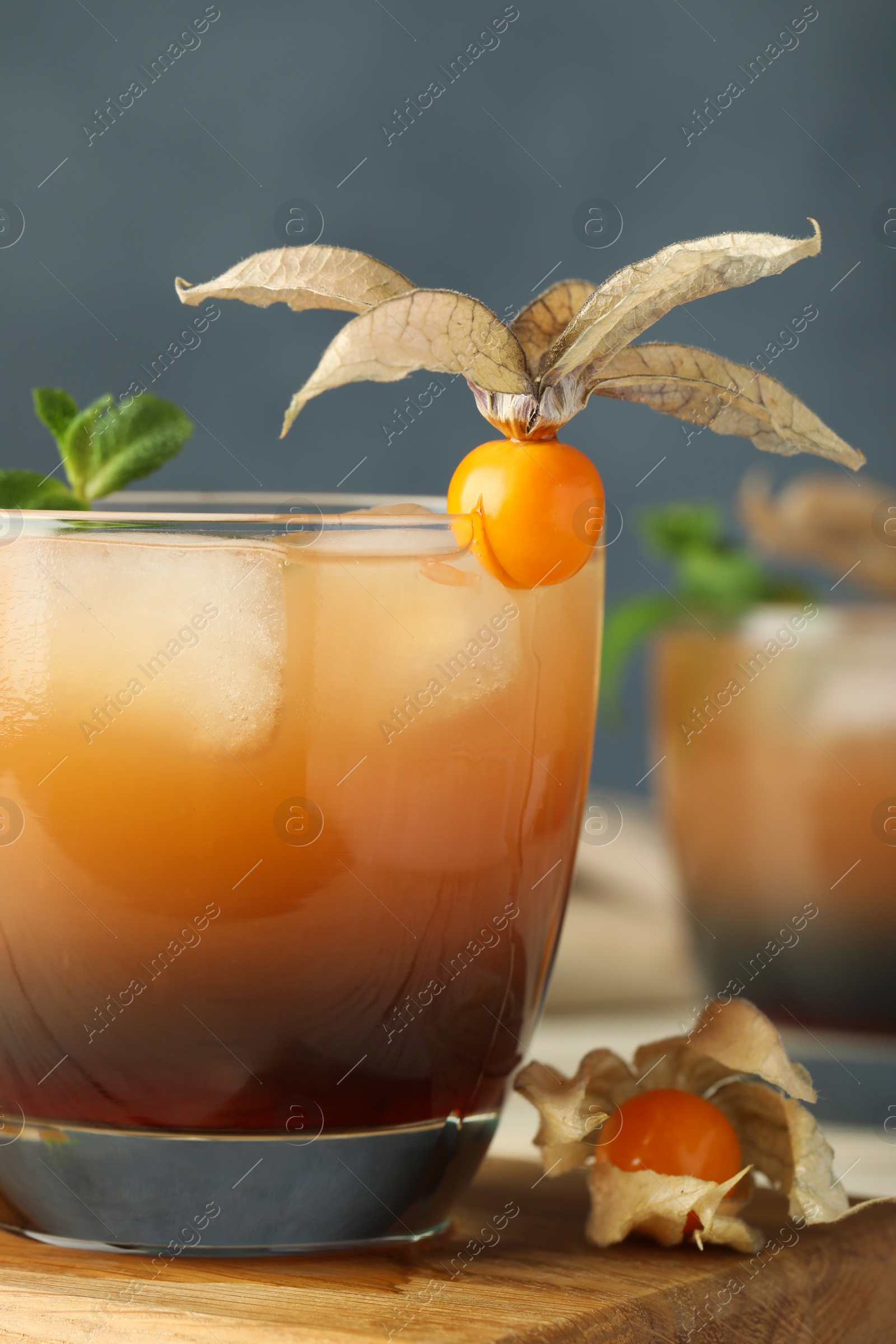 Photo of Refreshing cocktail decorated with physalis fruit on wooden table against grey background