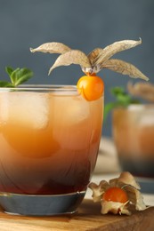 Photo of Refreshing cocktail decorated with physalis fruit on wooden table against grey background