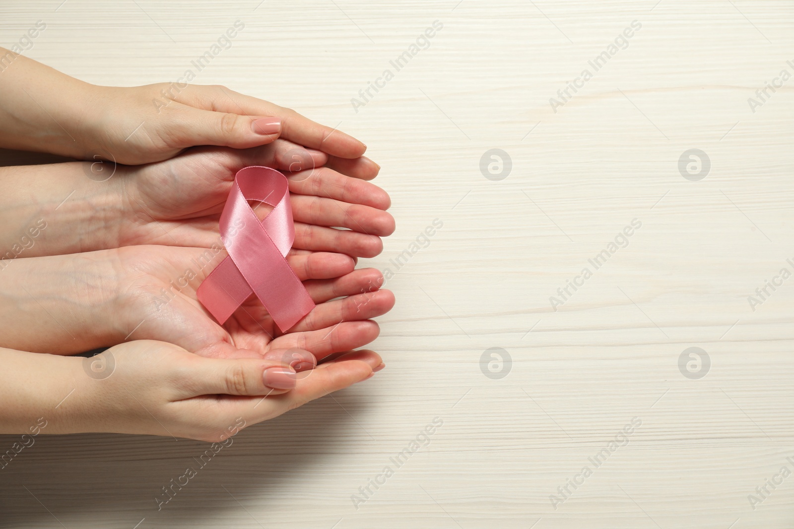 Photo of Breast cancer awareness. Women holding pink ribbon at white wooden table, top view. Space for text